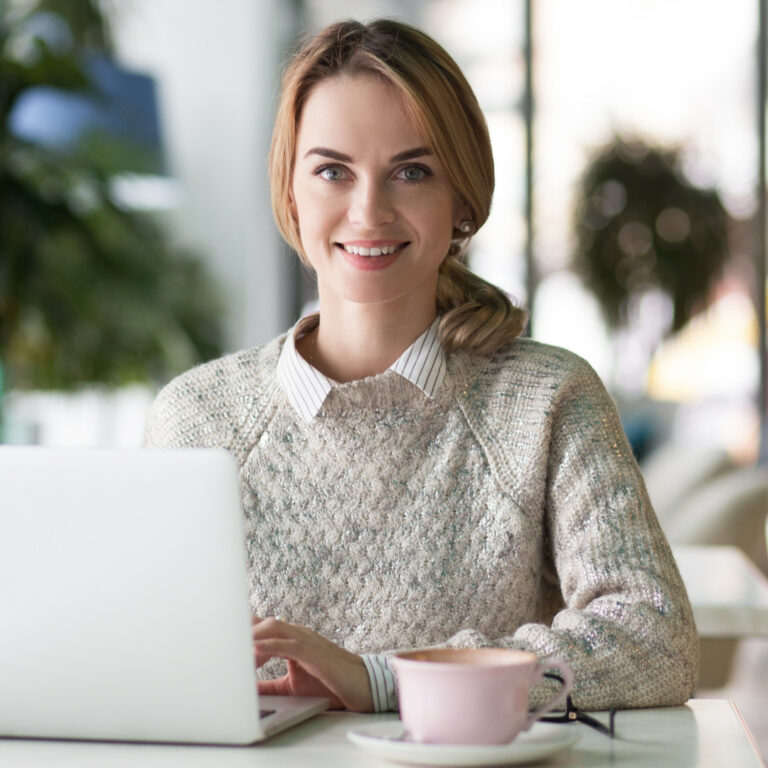 A smiling woman sitting at a table with a laptop.