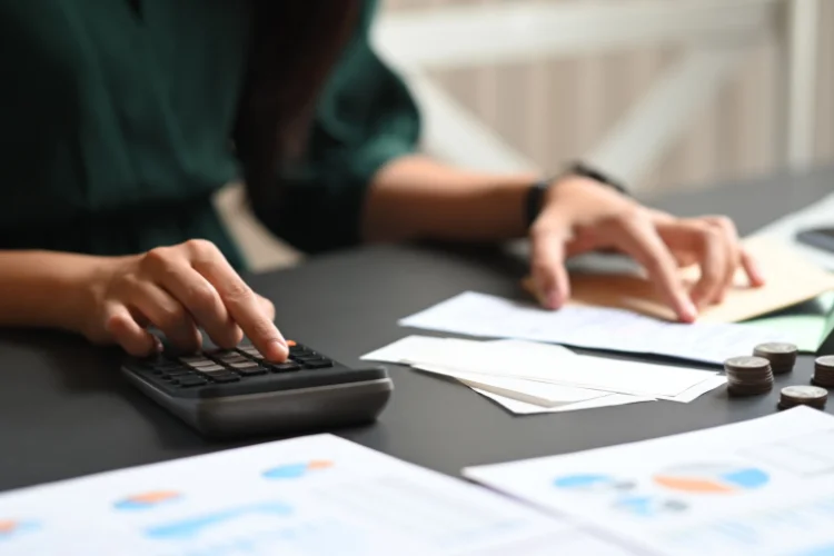A woman is managing expenses and receipts using a calculator while sitting at a desk. - JacRox